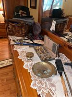 Wide view of dresser displaying the assembled collection showing basket with hats and assorted men's accessories including jewelry box with cuff links and tie pins, clothes brush, brass change tray, and resin candle holder on lace runner.