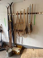 Wide angle showing the Kuusiston and Era-Finn cross-country skis, wooden snowshoes, lacrosse sticks, fishing rod and tackle box in garage setting.