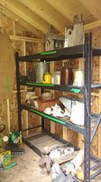Full view of black metal shelving unit loaded with garden pots and decorations inside a wooden shed
