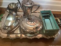 Overview of entire silverplate serving set on ornate tray including coffee pot, gravy boat, cream and sugar pitchers, and carving aid in box