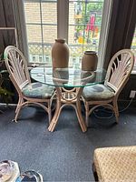 Full view of glass tabletop with bamboo and wicker base and two matching chairs with patterned cushions near windows.