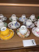 Photo showing 11 teacups and matching saucers in various colors and floral designs displayed on a wooden surface.