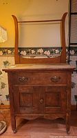 Front view of vintage wash stand showing drawer with metal hardware, cupboard doors, and curved back frame with horizontal rod