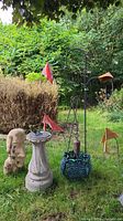 Overview of all yard ornaments on grass: sundial, bust, planter, wind spinner, shepherd’s hook with cowbell