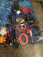 Full view of compressor, battery charger, extension cords, jumper cables, stands, oilers and lenses on blue tarp