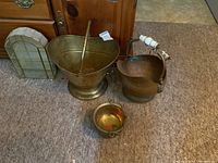 Overview of the full lot showing brass ash bucket, copper pitcher, small brass plant pot, and glass/metal display shelf