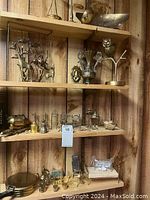 Three wooden shelves displaying various brass figurines, an urn, owl on branch, and some dollhouse furniture pieces including beds and chairs.
