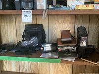 Wide view of shelf showing Polaroid camera, flash, camcorder, binoculars and cases
