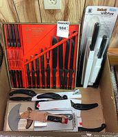 Full view of Northcraft Wellington Swords knife set in orange case, Wiltshire StaySharp self-sharpening knife set in packaging, ulu blade in sheath, cleaver blade, and black handled kitchen knives and tools.