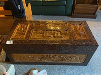 Full view of the top and front carved design of the wooden chest, highlighting intricate patterns and scenes.
