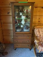 Full front view of oak cabinet showing glass door, drawers and interior shelves filled with contents