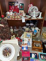 Shelving unit with assorted holiday and Christmas-themed decor including mugs, angel figurines, pinecone tree, decorative plates, napkins, and glassware
