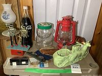 Wide shot showing various vintage collectibles including Coke bottle, red lantern, glass bear jar, metal windup toy, eyeglasses, coasters, and ceramic deer figurine.