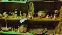 Top shelf and middle shelf with multiple copper and brass decorative items including candle holders, small pots, bells, and plates.