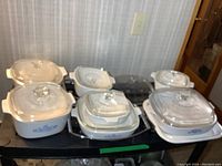 Photo showing full set of CorningWare blue cornflower baking dishes with lids arranged on a black surface.