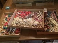 Overview of three boxes filled with assorted beads, necklaces, brooches and chains