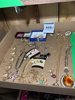 Photo showing a tray filled with assorted costume jewelry items including earrings, necklaces, pins, and a watch.