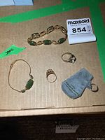 All four jewelry pieces laid out on cardboard background with auction label and green tape labeled Jade.