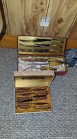 Photo showing two open boxes: one contains four steak knives with patterned darker handles, the other contains four knives with lighter handles.