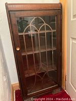 Front view of closed cabinet showing decorative glass door with arched mullions and wood finish