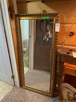 Full view of large rectangular gold framed mirror standing against wall, showing overall condition and size.