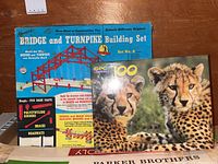 Photo showing Kenner Bridge and Turnpike Building Set box and GPC 100-piece cheetah puzzle box on wooden surface.