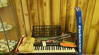 View showing 60 key keyboard, violin, music stand, and music books on a wooden floor with wood paneling background.