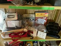 Full view of kitchen appliances including boxed microwave egg poacher, menu hot plate, Toastess deep fryer, fat grilling machine and accessories on a shelf.