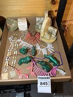 Tray with marble bookends, pencil holders, carved stone necklaces, and small animal figurines arranged on a wooden surface.