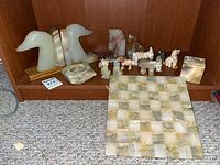 Shelf showing marble loon bird bookends, marble ash tray, various small animal carvings, and marble chess board with pieces.