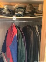 Closet shelf with men's and ladies' jackets hanging, including a red and blue windbreaker and dark leather and suede jackets.