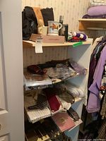 Four white shelves holding men's clothing and accessories including ties, scarves, shirts, slippers, suspenders arranged in a closet space with floral wallpaper.