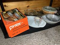 Photo showing boxed Pyrex Autumn Harvest 2-piece casserole set and several loose Pyrex baking dishes including round and oval with lids, clear glass bowl, and white plate.