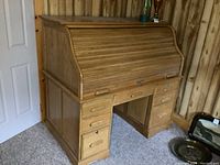 View of the front and right side of the roll top desk showing curved tambour roll cover and drawers.