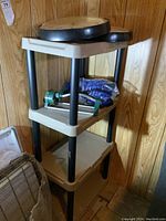 Plastic shelving unit with four shelves against a wood-paneled wall, showing two large round clocks on the top shelf.