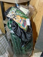 Side view of green sleeping bag with hot hood packed in black storage sack, partially wrapped in plastic.