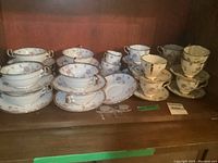 Wide shot showing all items in set including soup bowls, plates, cups, saucers, and cream and sugar containers in wooden cabinet.