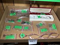 Overview of sterling silver jewelry lot in cardboard box with multiple plastic bags containing chains, pendants, earrings, and brooches. Includes a pink marbled bracelet.