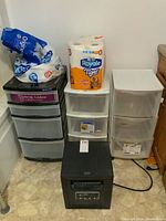 Photo showing three plastic drawer units, two bags of toilet paper on top, and the heater in front on floor.