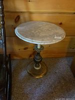 Full view of the small round side table with marble top and brass base next to wooden wall.