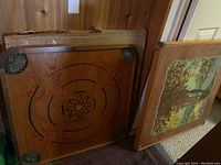 Vintage double-sided wooden game board leaning against wall showing crokinole side with concentric rings and netted corners.
