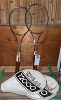 Two Wilson T2000 tennis rackets leaning against wooden background with two white Wilson covers placed in front, showing condition and overall look.