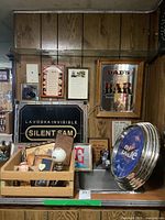 Overview photo showing most items in the lot including framed mirror signs, prints, wooden crate with lamp ornament, and metal trays.