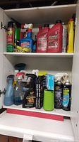 Two shelves inside a cabinet with assorted car care fluids and insect repellents. Includes multiple red Kendall oil bottles, spray bottles, and cans.