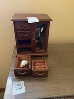 Wooden jewelry box on a table with two drawers open showing costume jewelry inside.