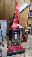 Full view of Dirt Devil Envision upright vacuum showing red body, black hose attachment, and clear dust bin with visible dirt.