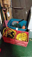 Two red milk crates filled with yellow and orange electrical extension cords. A blue tote containing string lights and an orange bug zapper racket on top.