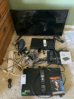 RCA TV, Philips DVD player, Sony Blu-ray player, LG DVD player, Panasonic phones, and power bar laid out showing remotes, cords, and manuals