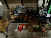 Wide view showing multiple cribbage boards stacked, playing cards, dice, poker chips on carpeted floor under table