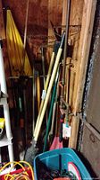 Full view of garden and yard tools leaning against wall in shed, including umbrellas, rakes, shovels, and post hole diggers.